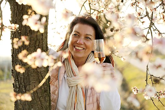 Frau mit einem Glas in der Hand unter einem Mandelblütenbaum